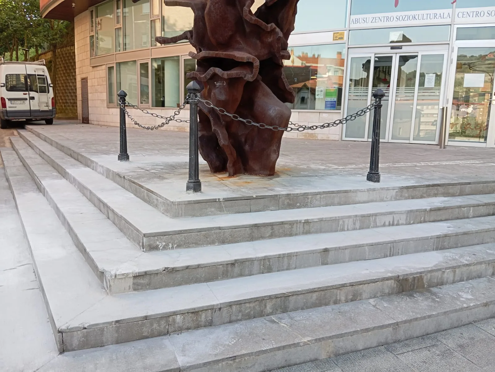 Bolardos negros unidos por cadenas alrededor de una escultura en una plaza