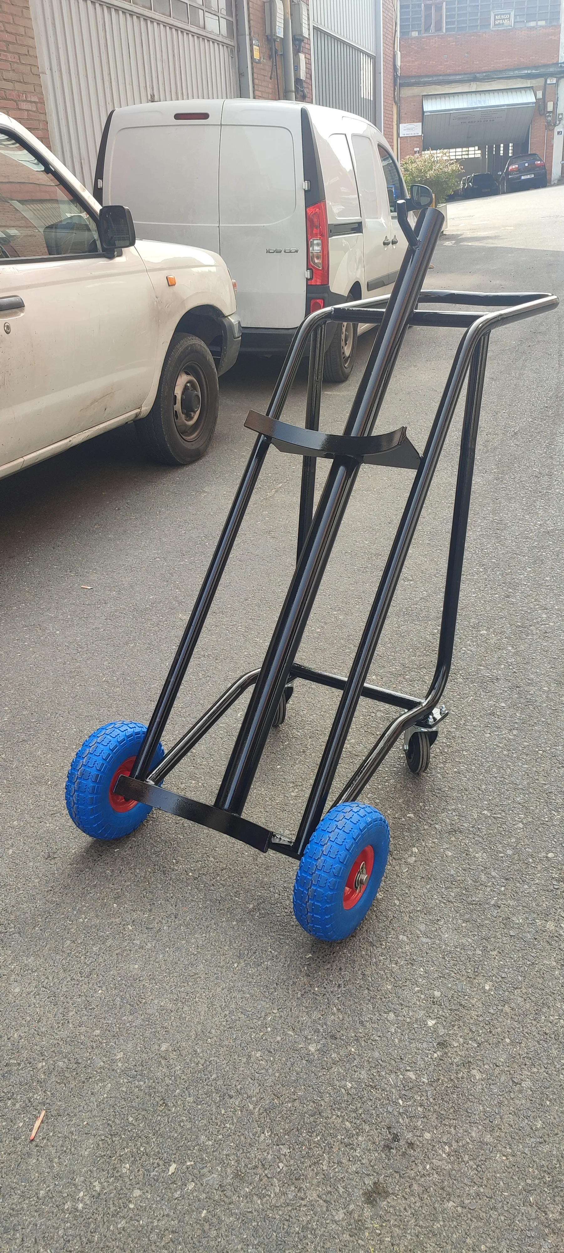 Carro metálico negro de dos ruedas azules apoyado en la calle