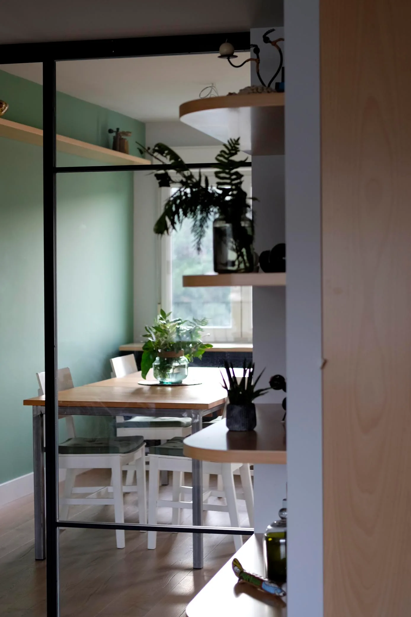 Cerramiento de perfiles negros y vidrio con vistas a un comedor de pared verde