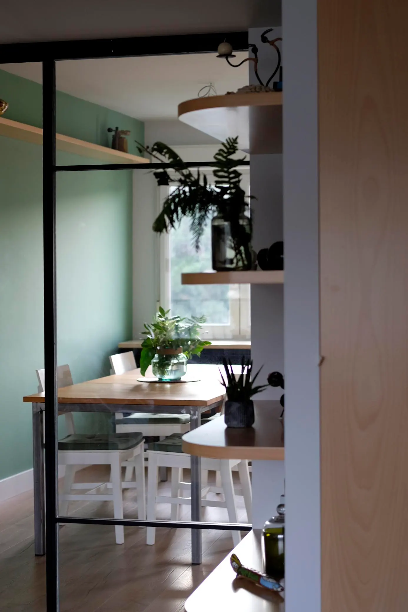 Cerramiento de perfiles negros y vidrio con vistas a un comedor de pared verde