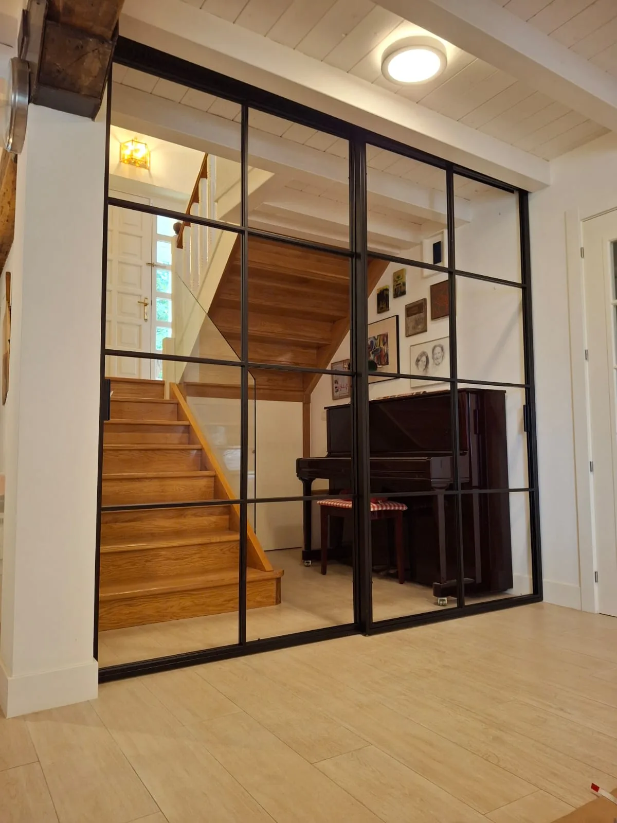 Cerramiento negro acristalado entre una estancia y una escalera de madera