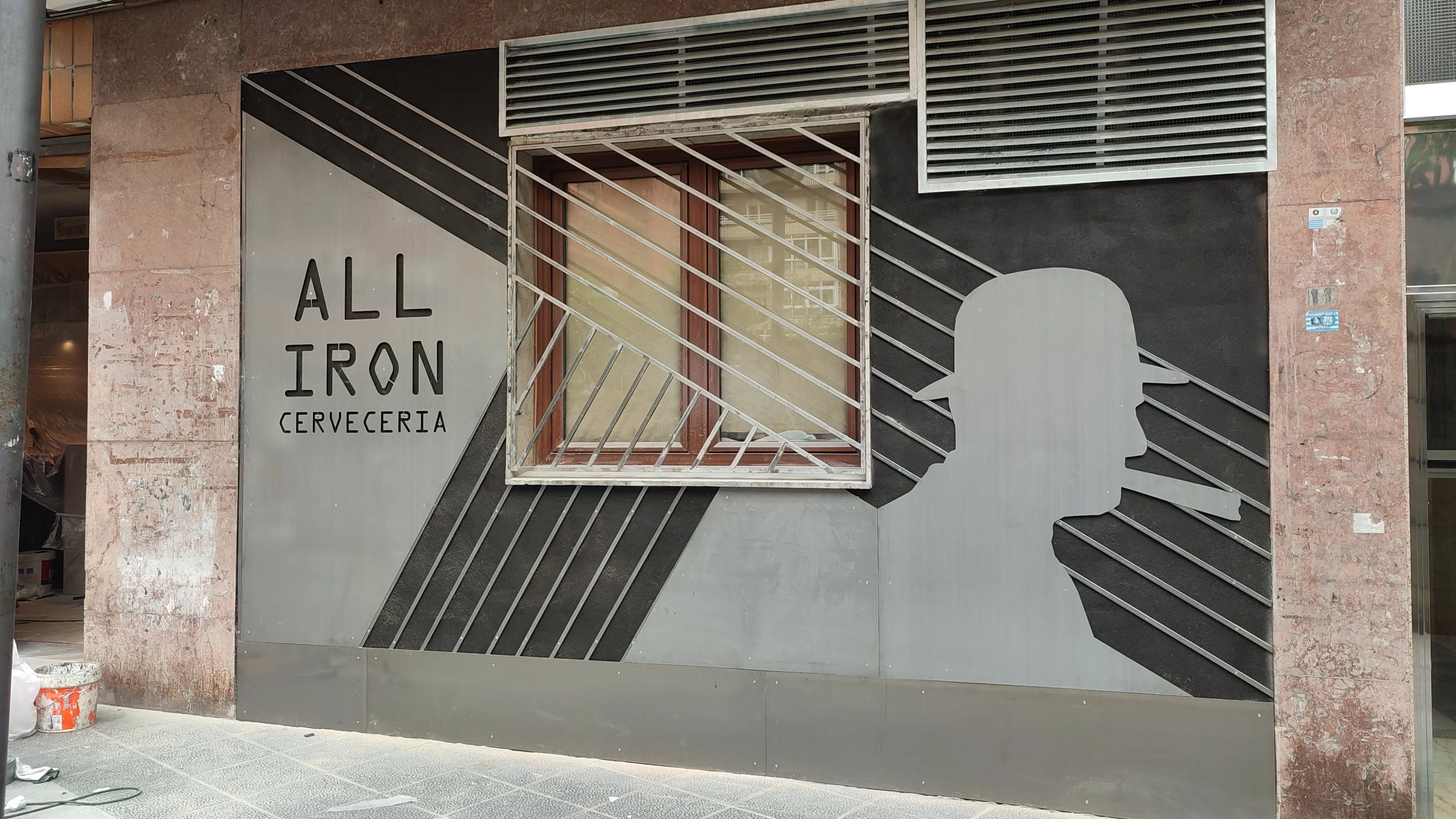 Fachada de local revestida de chapa gris oscura con siluetas y rejilla sobre la ventana