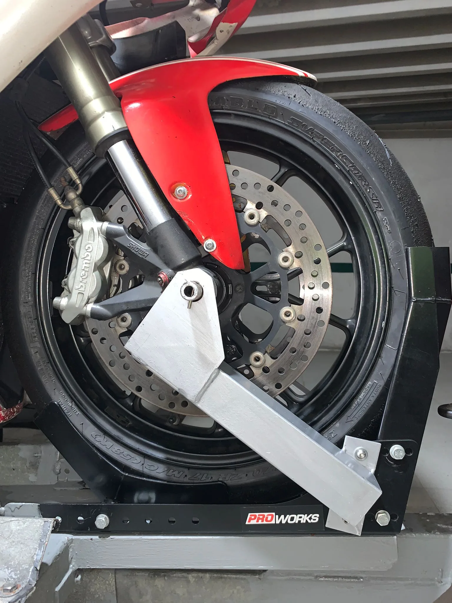 Soporte metálico gris sujetando la rueda delantera de una moto roja